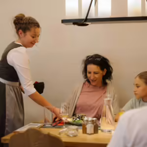 Servicefachfrau serviert einem Gast einen Salat